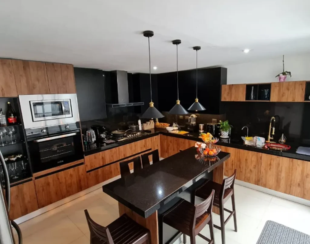 Cocina en tonalidades oscuras, con mesa café en el centro y lámparas colgantes son una de las mejores ideas de quienes no saben cómo decorar una cocina.